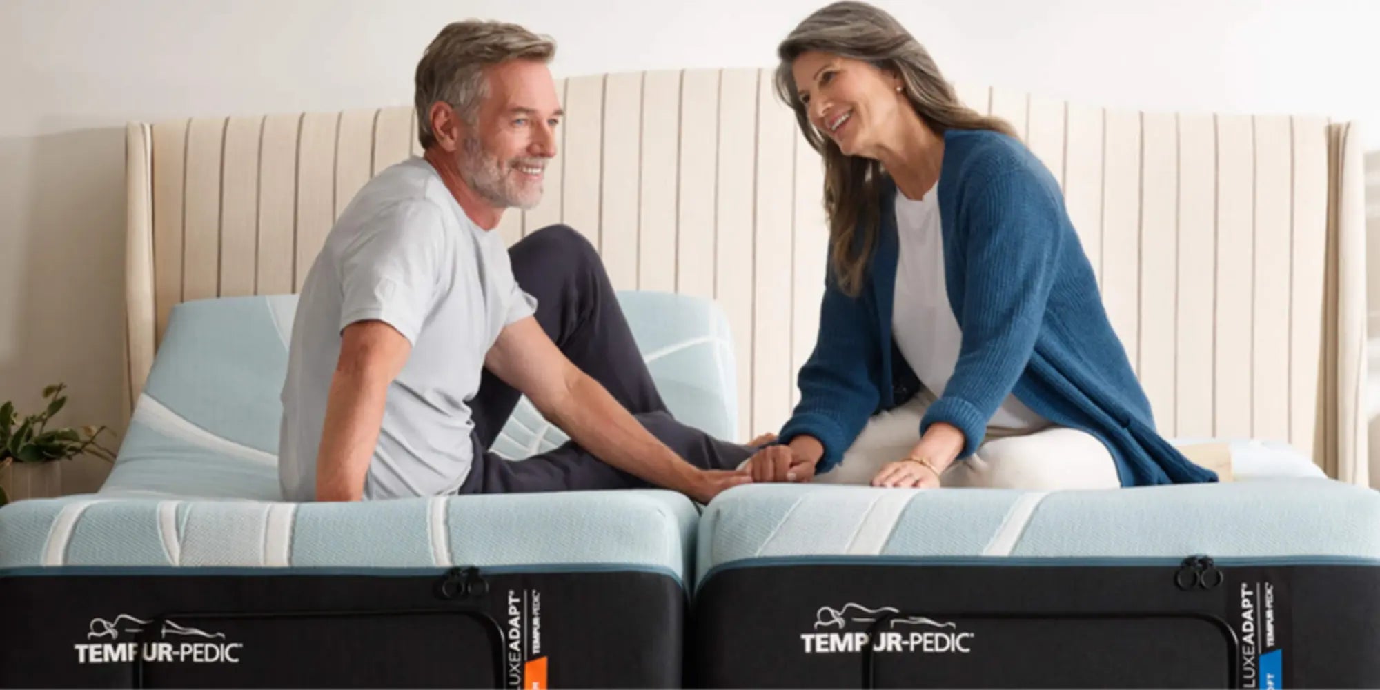 Man and woman sitting on a Tempur-Pedic mattress, smiling at each other.